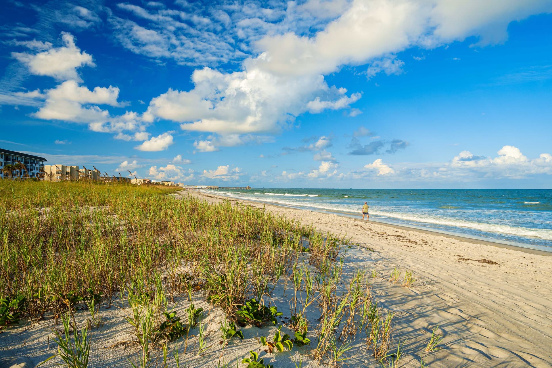 Cocoa Beach shoreline with sea grass dunes, white sand, and turquoise Atlantic waves under blue sky