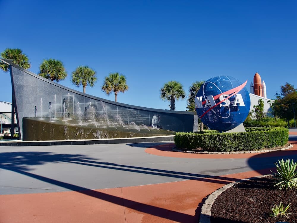 NASA globe entrance at Kennedy Space Center Visitor Complex with fountain wall and palm trees